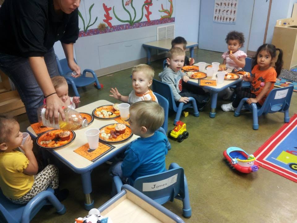 Person pouring drinks for children seated at tables in a classroom