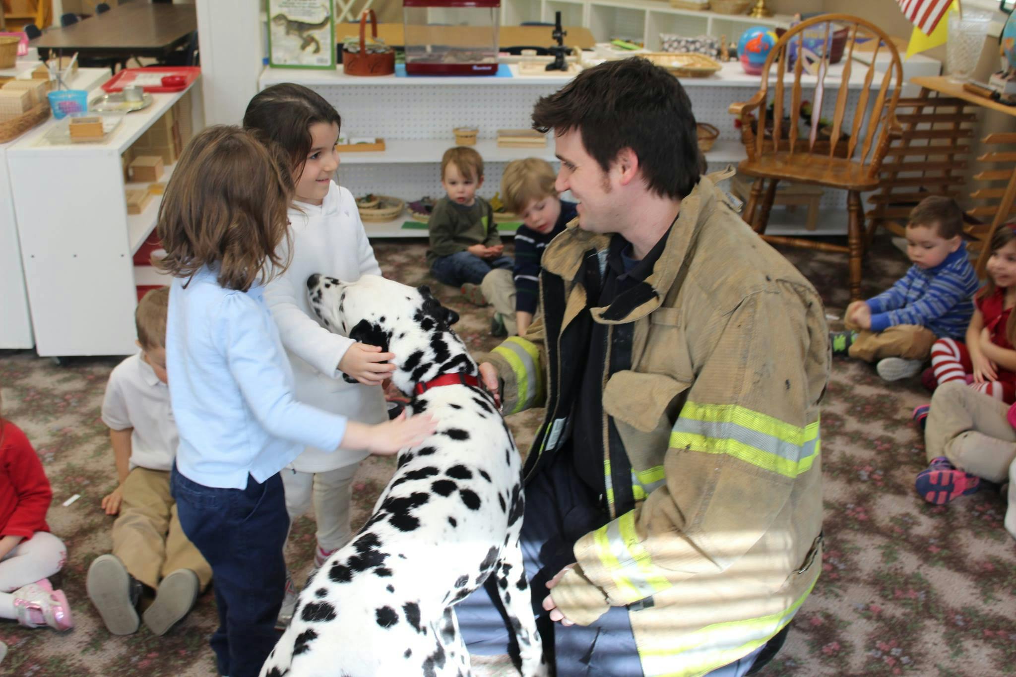 Person in firefighter gear with children petting a Dalmatian dog