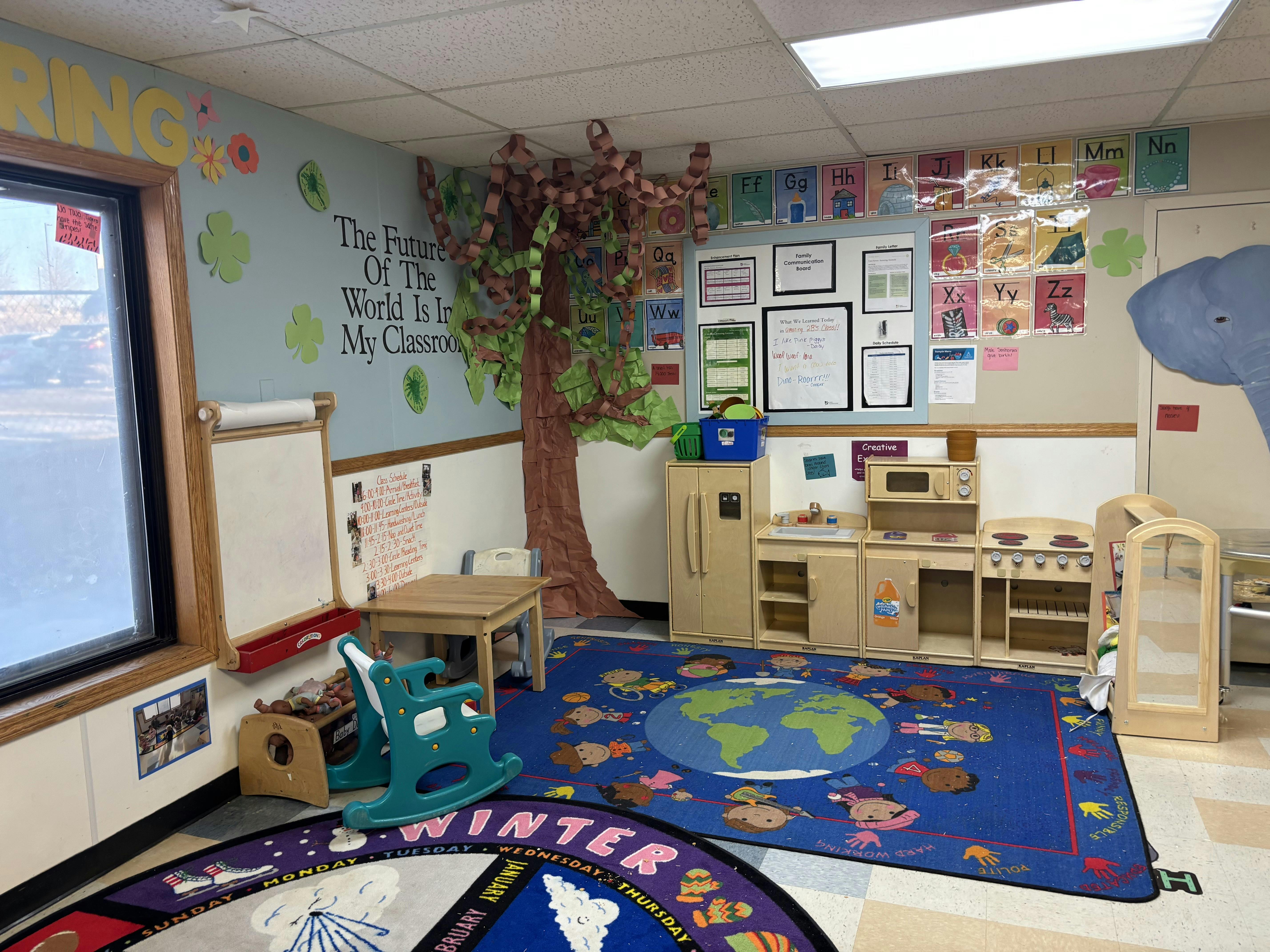 A classroom with a tree decoration, play kitchen, small table, and alphabet charts