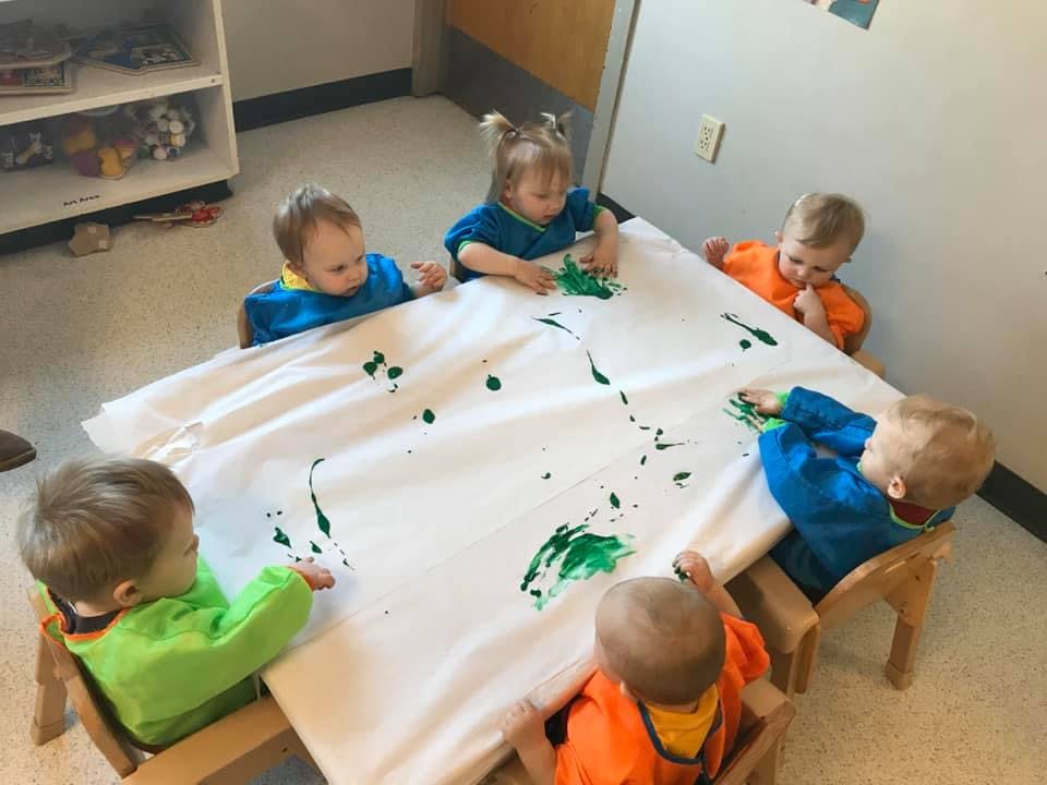 Five children finger painting with green paint on a white sheet
