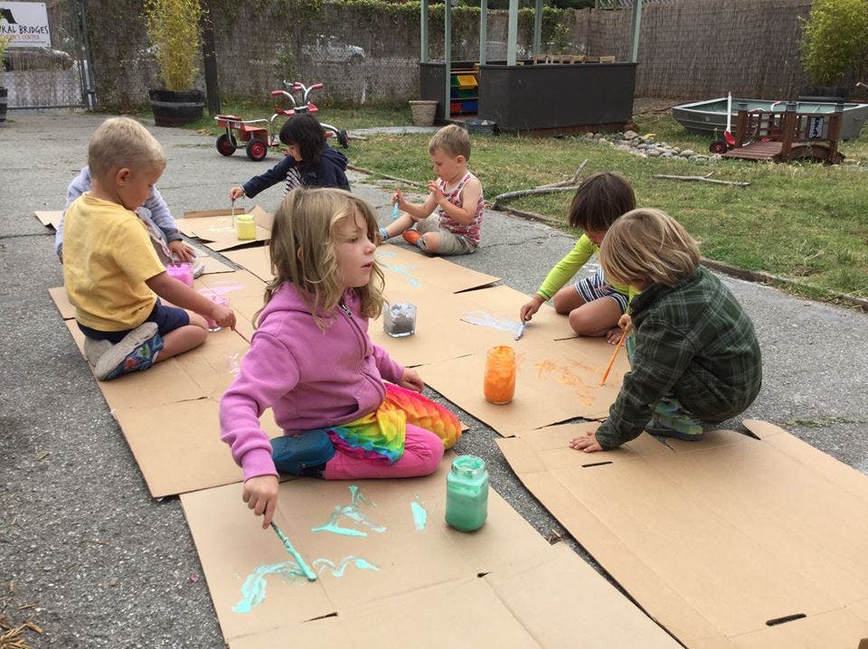 Children painting on cardboard outdoors