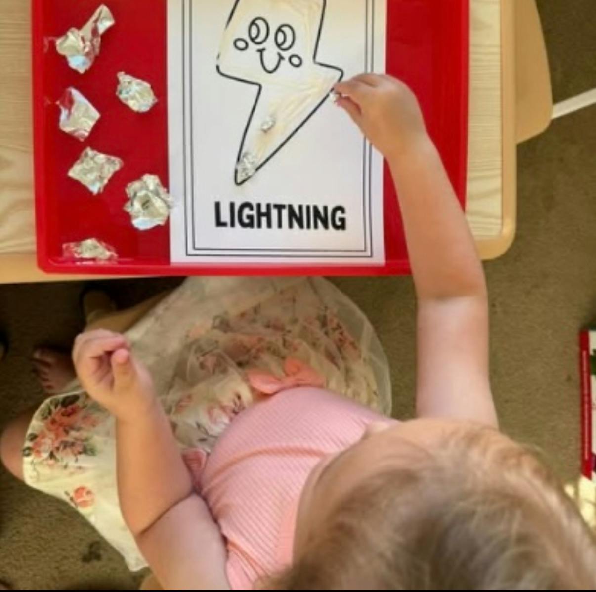 Child placing crumpled foil on a lightning bolt drawing labeled "LIGHTNING"