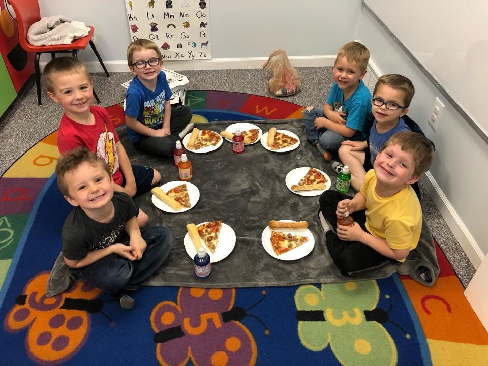 Six children sitting on a rug eating pizza