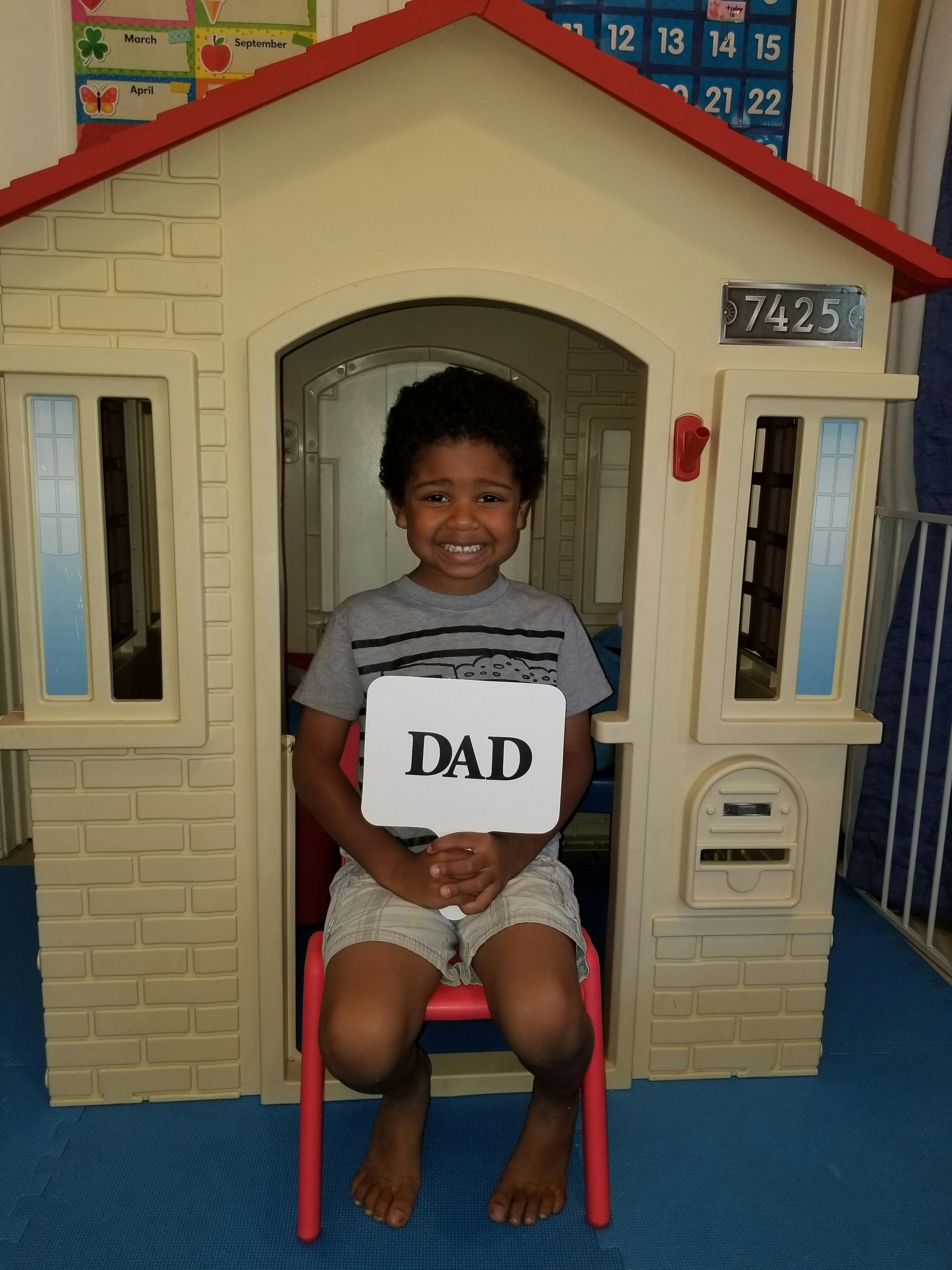 Child sitting in a playhouse holding a sign that says DAD