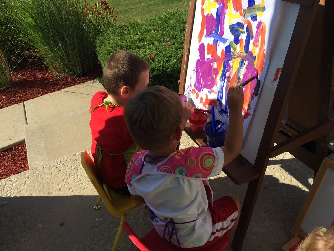 Two children painting on an easel outdoors