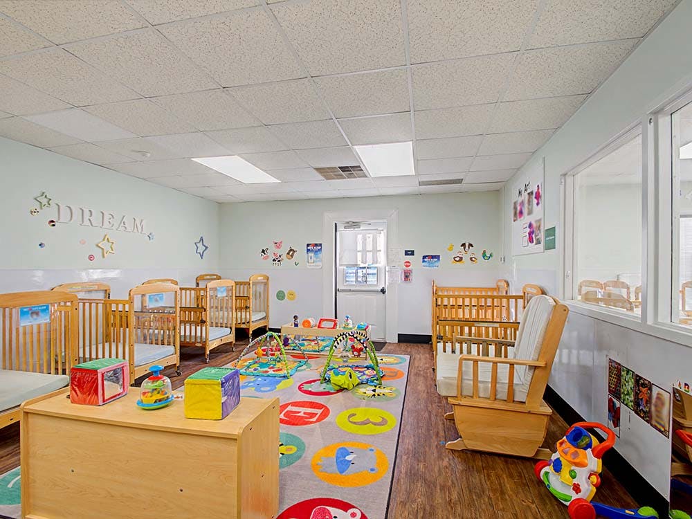 A colorful baby room with multiple wooden cribs and playmats on a patterned rug