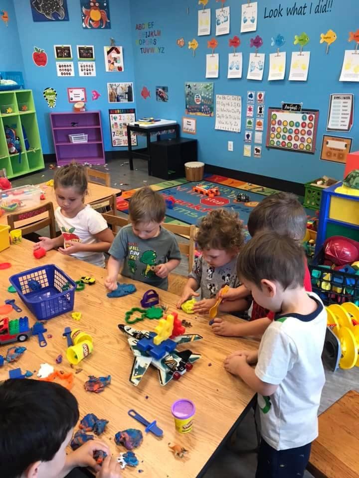 Children playing with modeling clay and toys at a table in a classroom