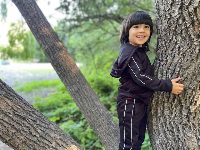 Child standing next to a tree trunk