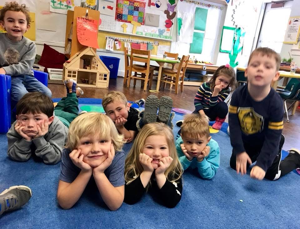 Group of children lying on a blue mat in a classroom