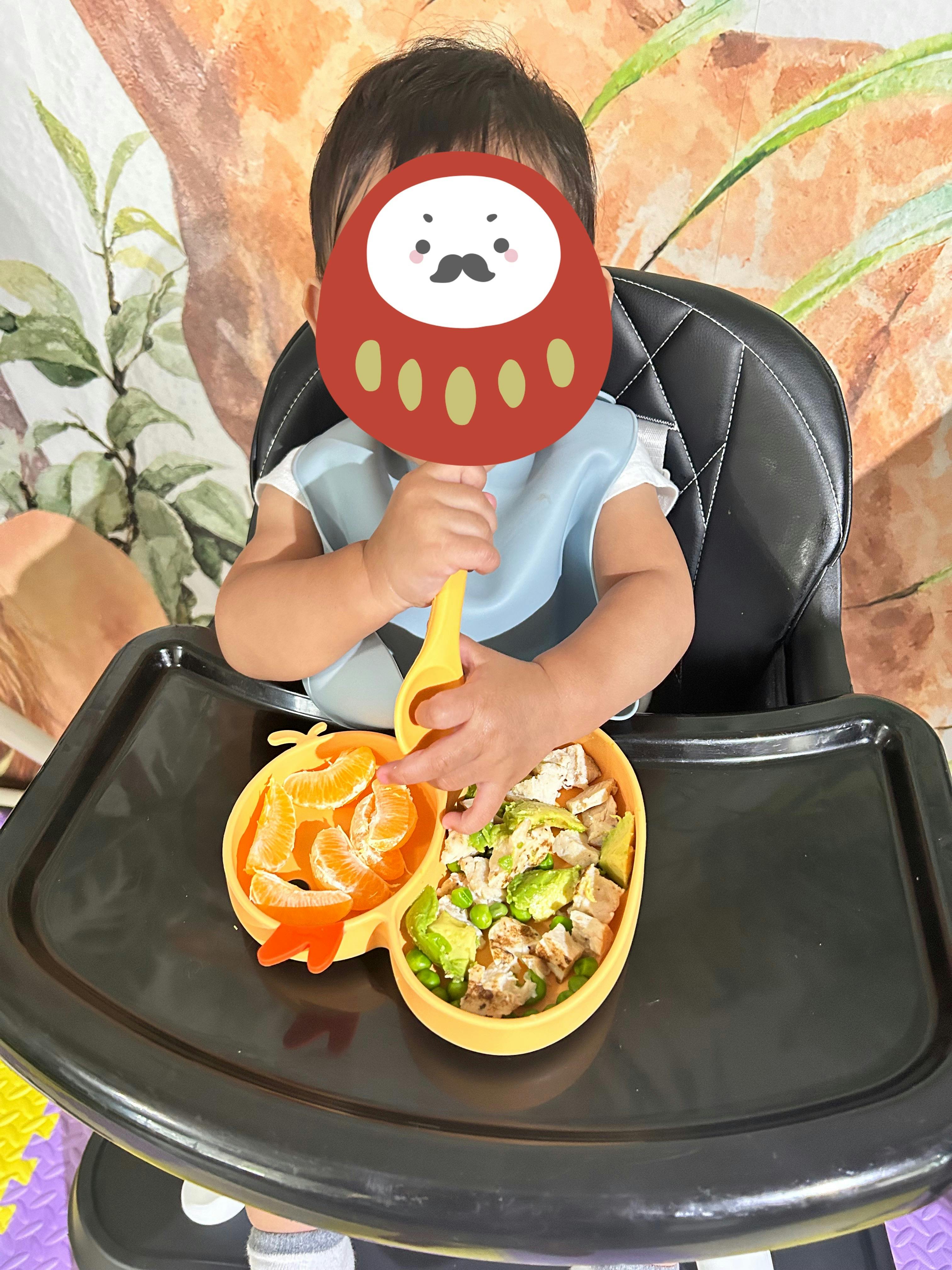 Child sitting in a high chair eating from a partitioned plate