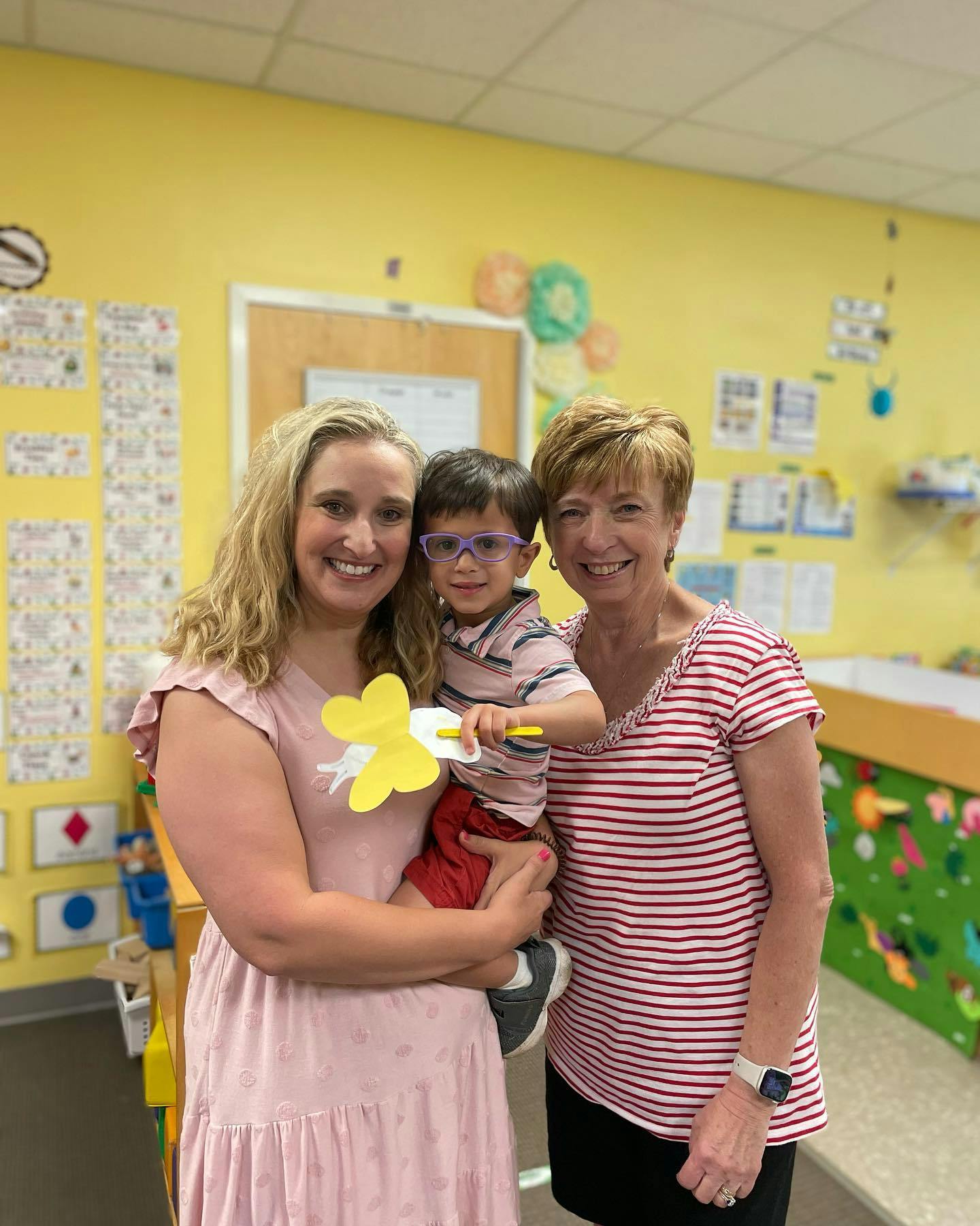 Two people standing with a child holding a yellow paper butterfly