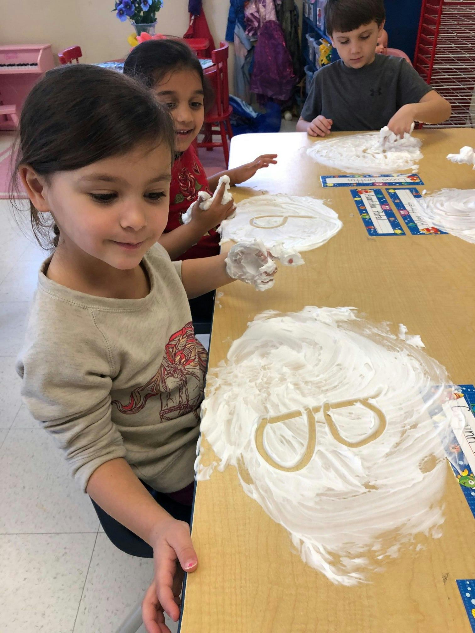 Three children playing with shaving cream on a table