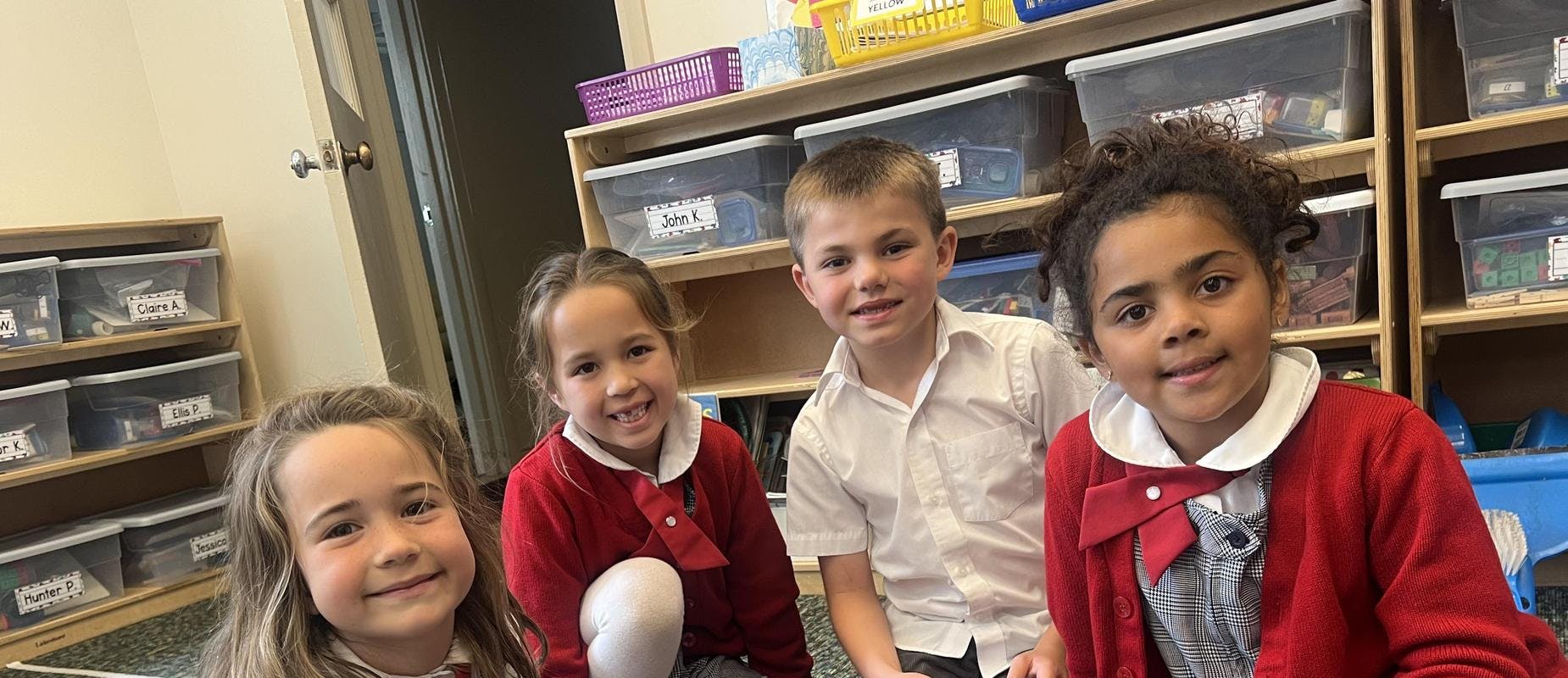 Four children sitting together in a classroom, smiling at the camera