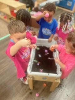 Children playing with sensory bin with dark material and small objects