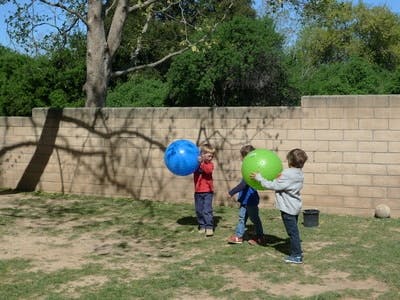 Three children playing with large balls outdoors