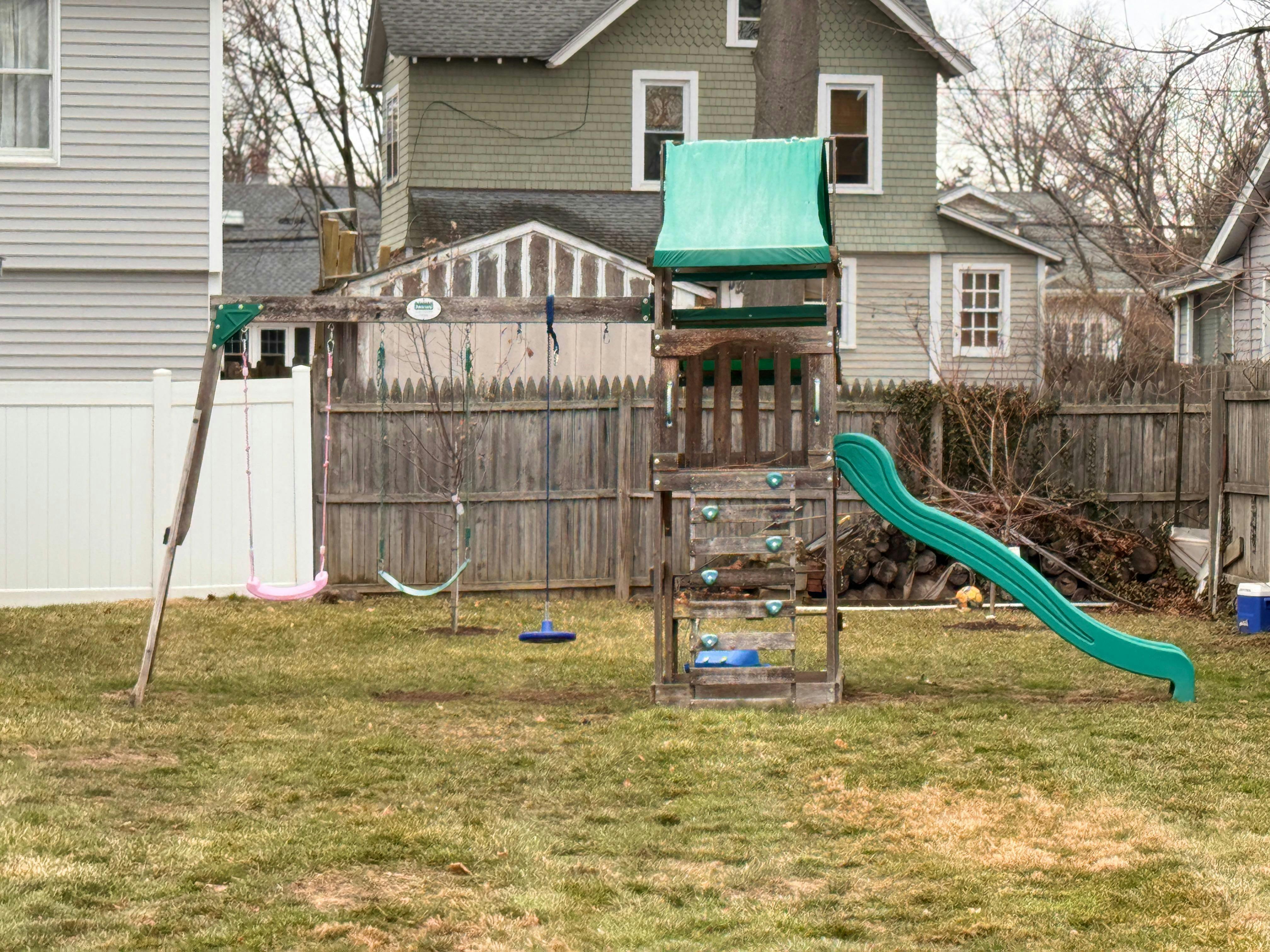 Backyard with a wooden playset, green slide, and swings