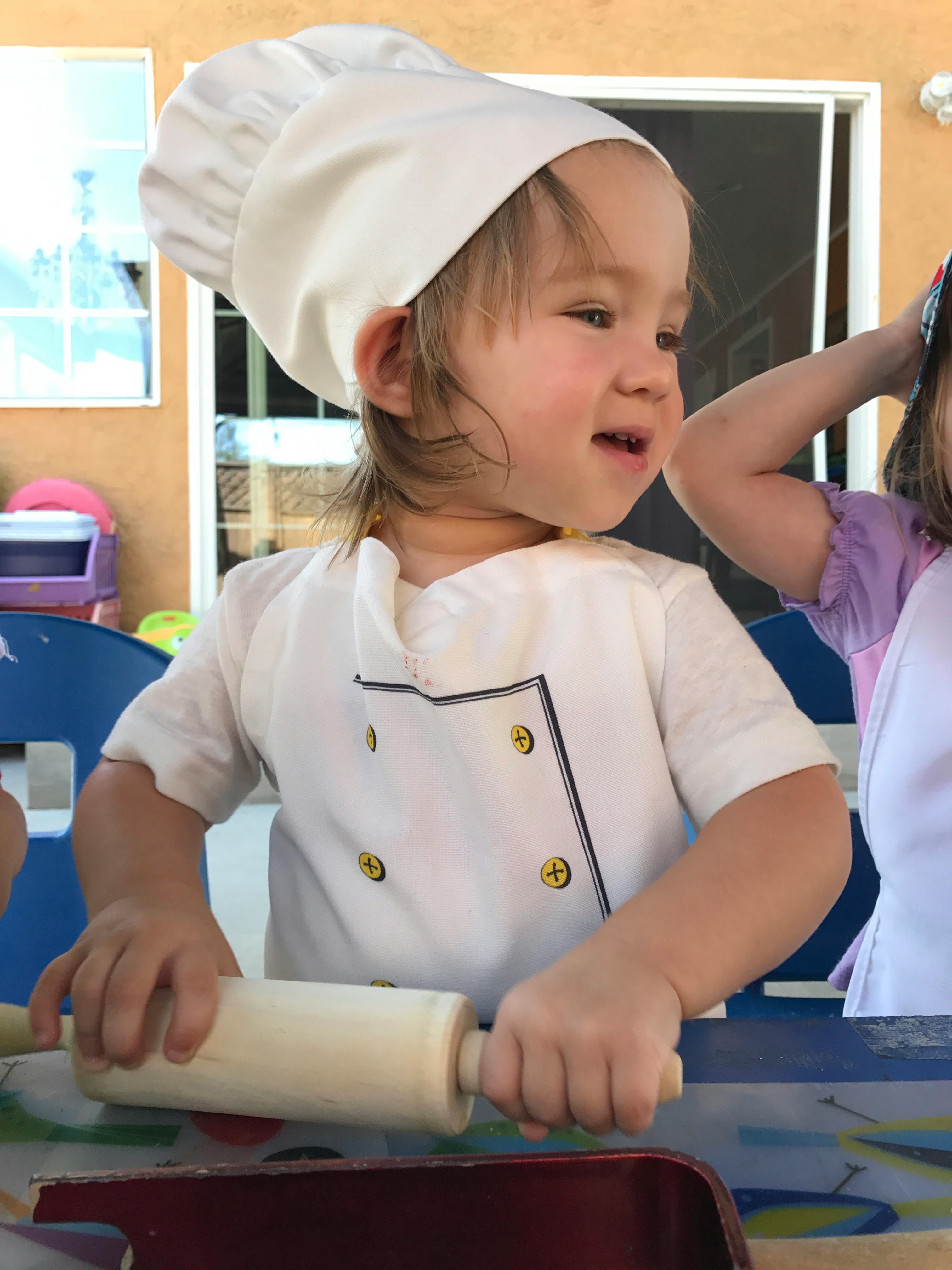 Child in chef's hat and jacket using a rolling pin