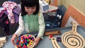 Child playing with colorful pom-poms and wooden toys