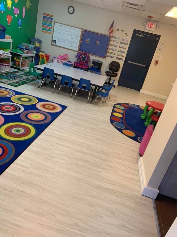 Classroom with small tables and chairs, colorful rugs, and a whiteboard