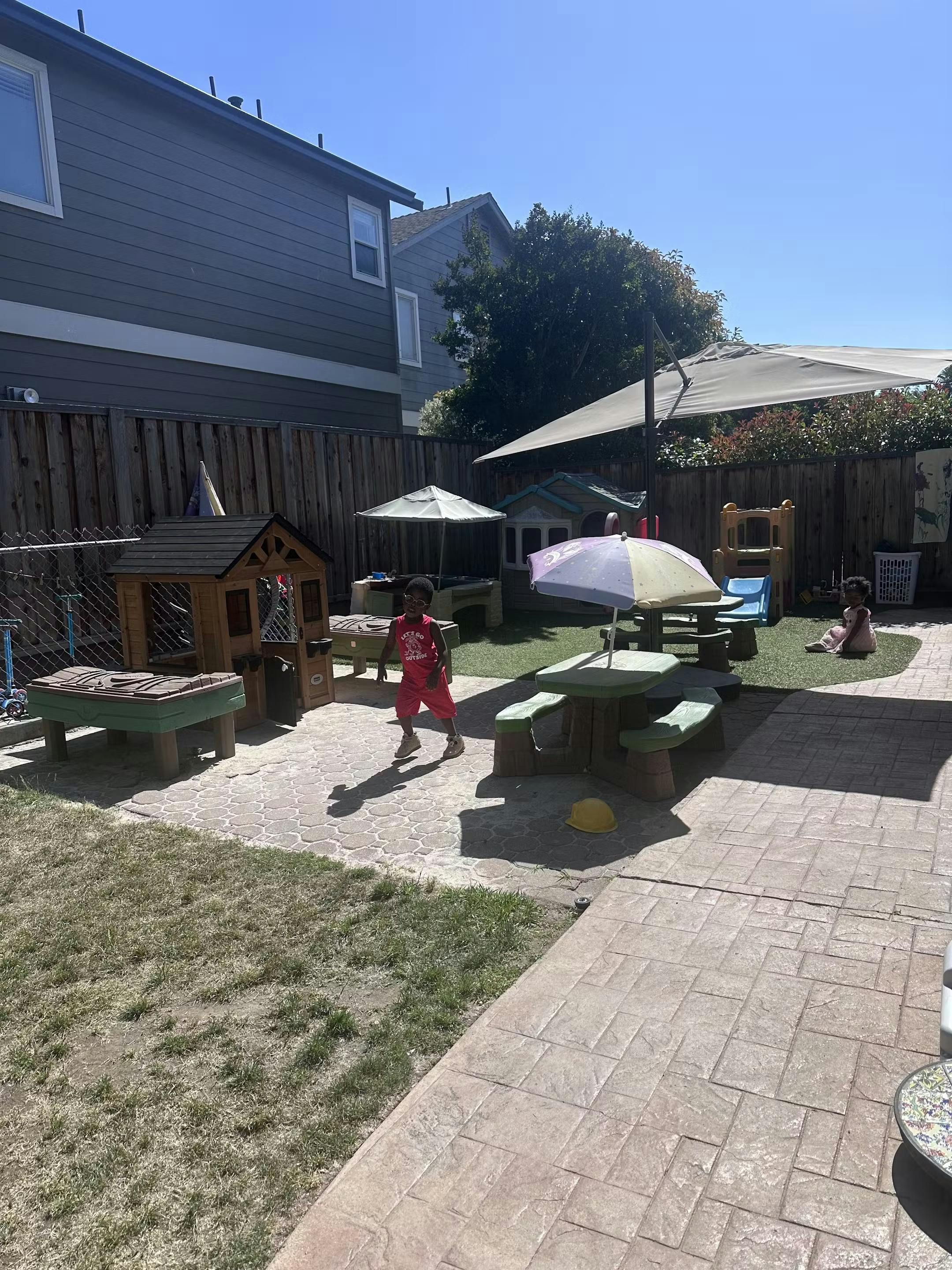 Child walking in a backyard play area with playhouses and picnic tables