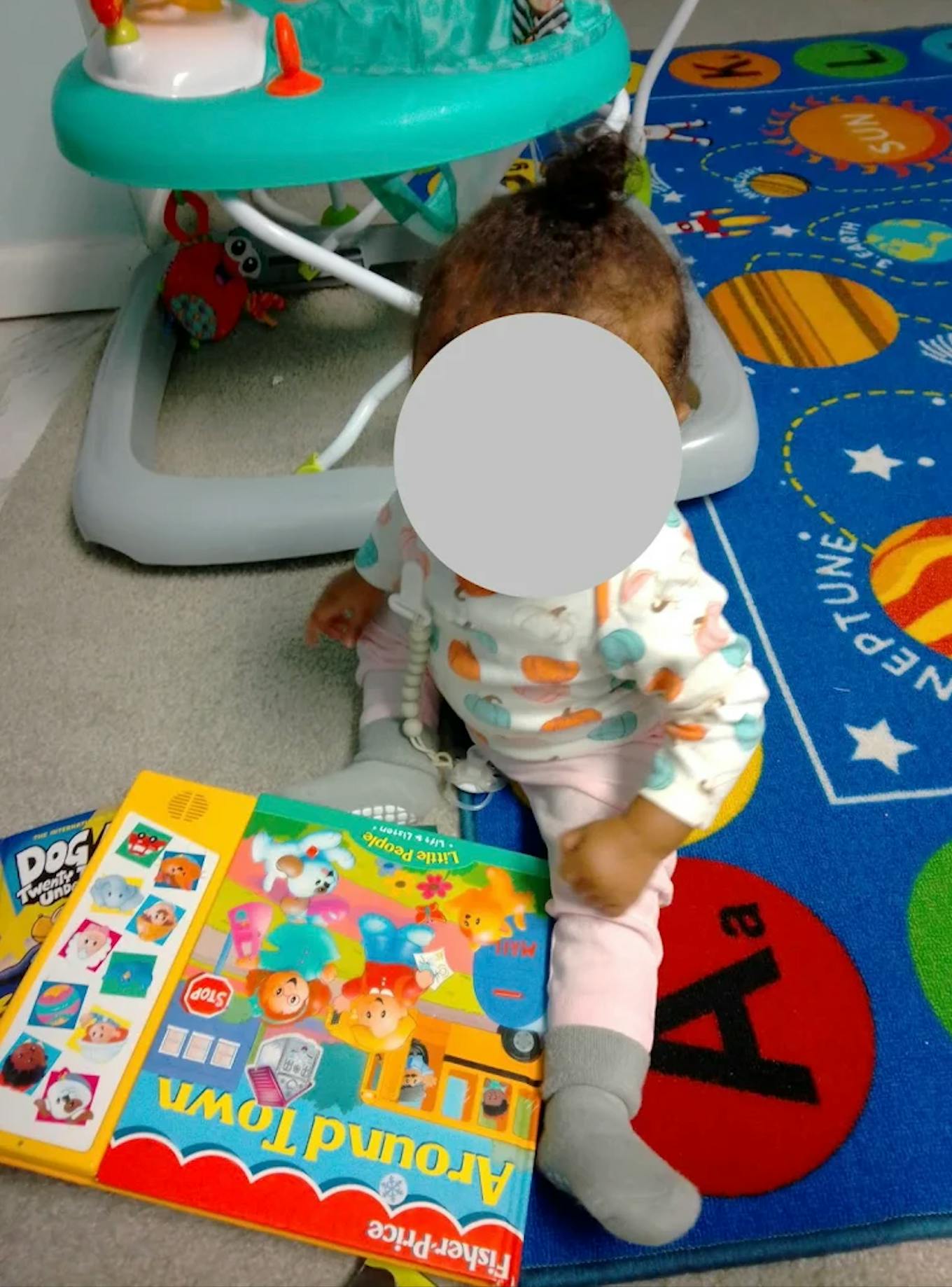 Child sitting on a planetary rug playing with a Fisher-Price sound book