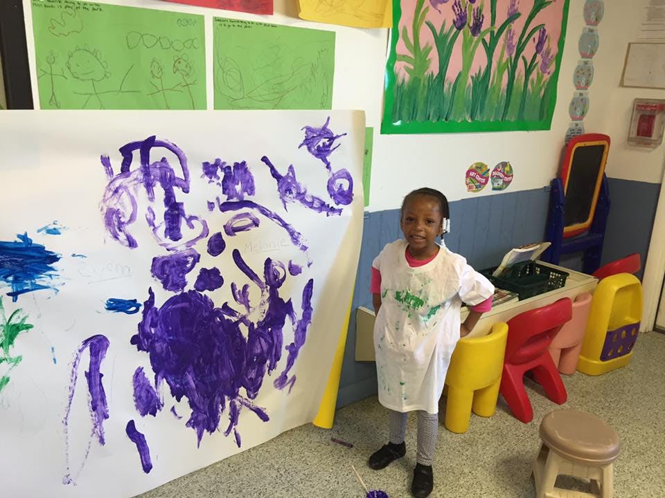Child standing next to a large paper with purple paint marks