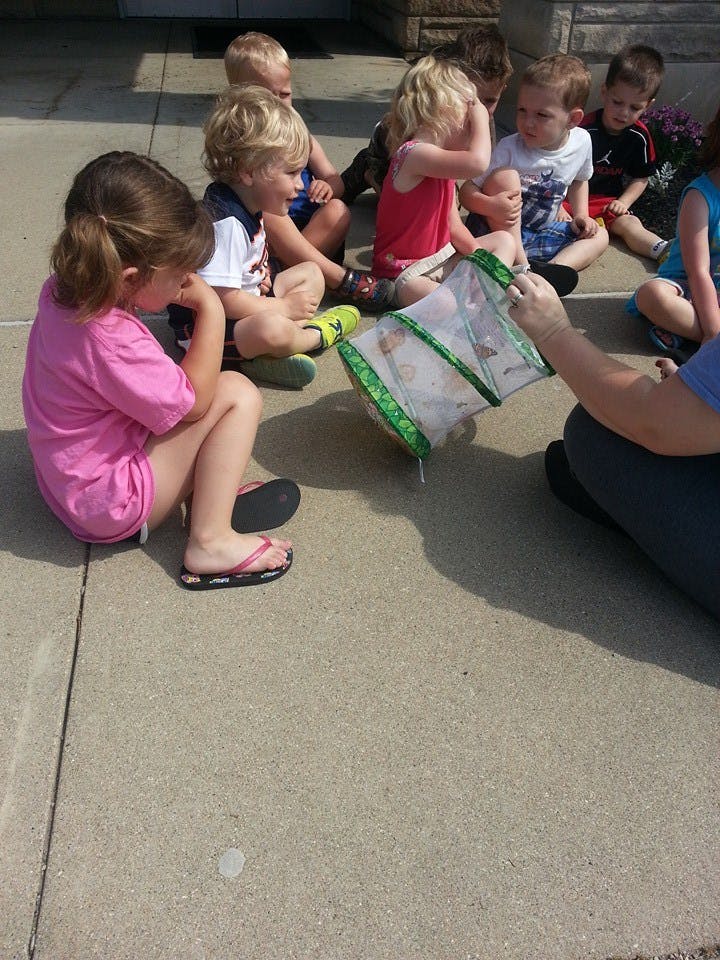 Children sitting on the ground looking at a mesh container