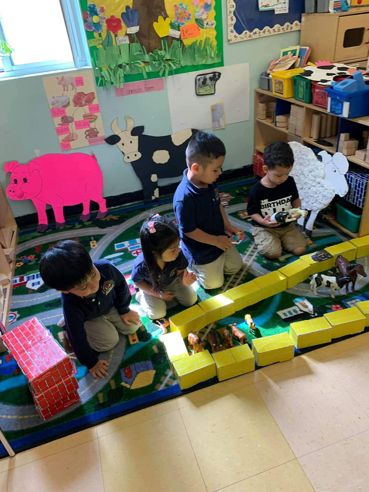 Children playing with blocks and toy animals on a rug in a classroom