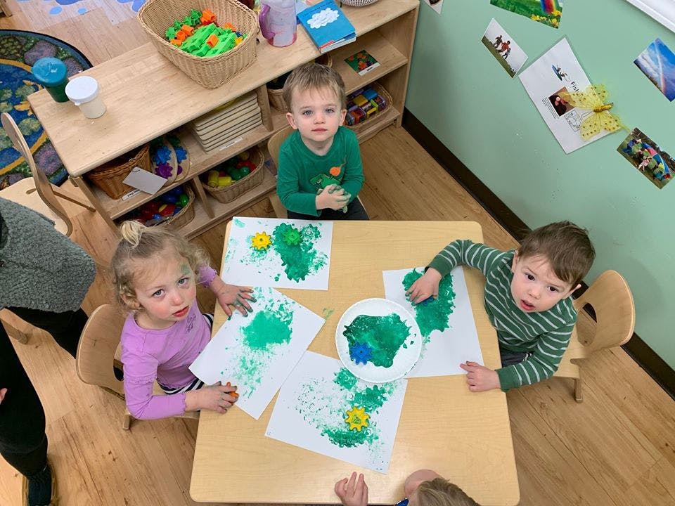 Three children painting at a table in a classroom