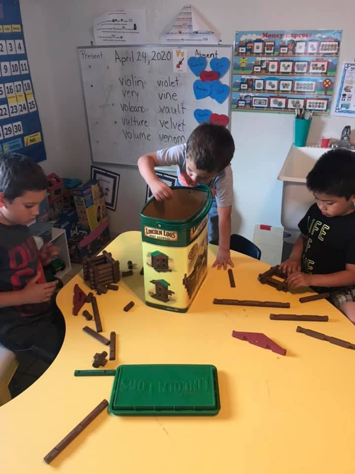 Three children playing with building blocks at a yellow table in a classroom