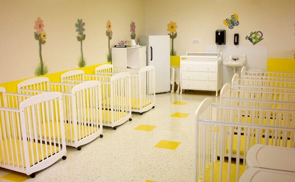 Room with multiple white cribs with yellow bedding