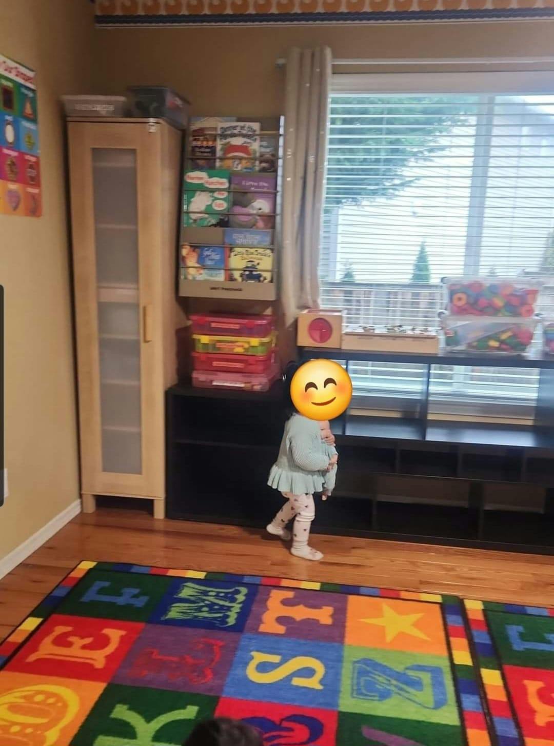 Child standing on a colorful alphabet rug in a room with shelves and a window