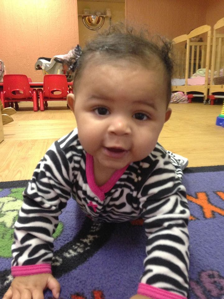 Child crawling on a rug in a room with cribs and small chairs