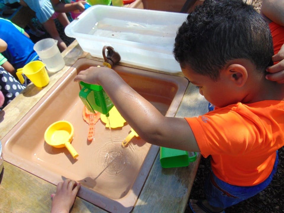 Child pouring water from a green container into a water table