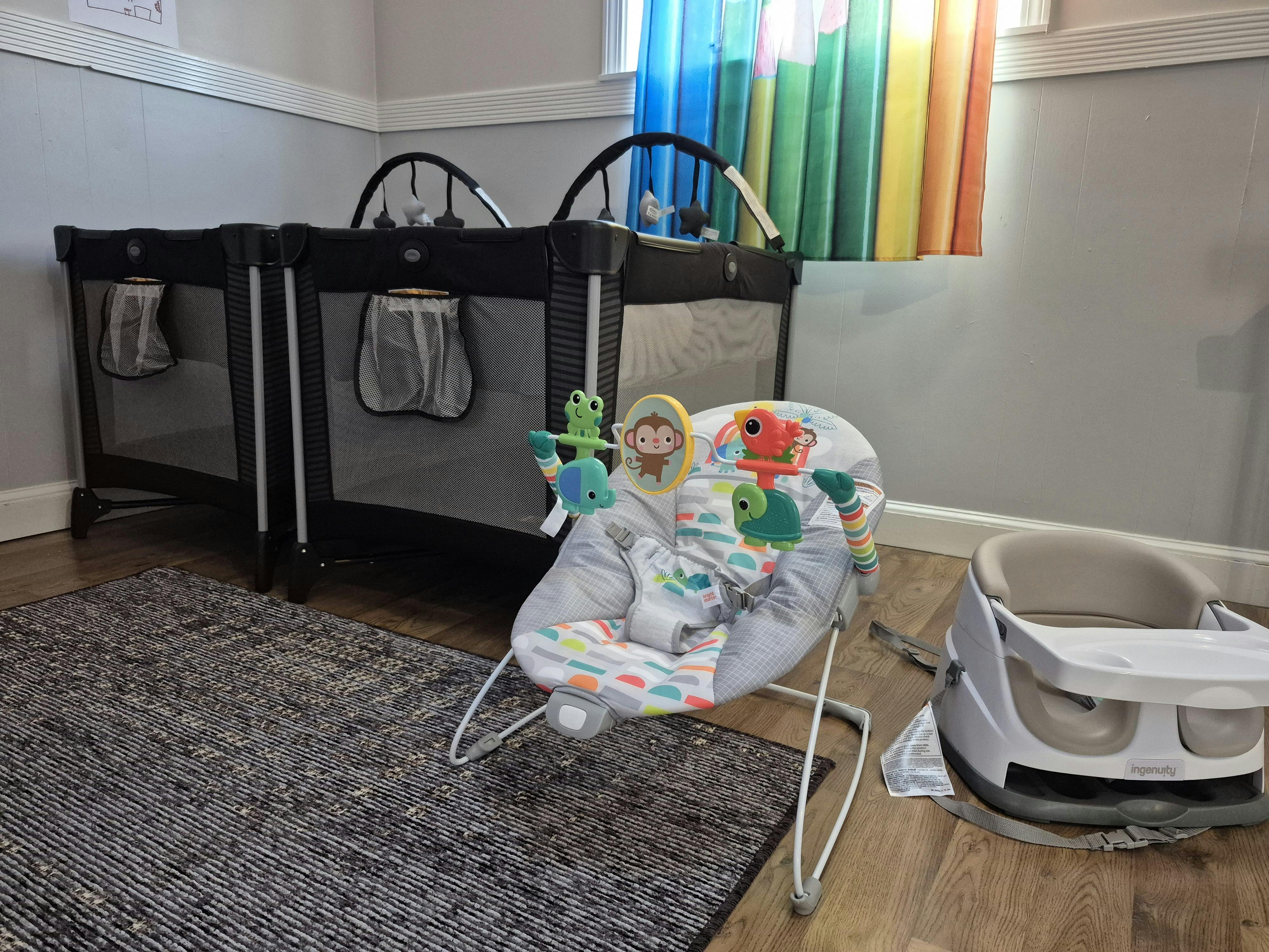 Two portable cribs, a baby bouncer, and a booster seat in a room