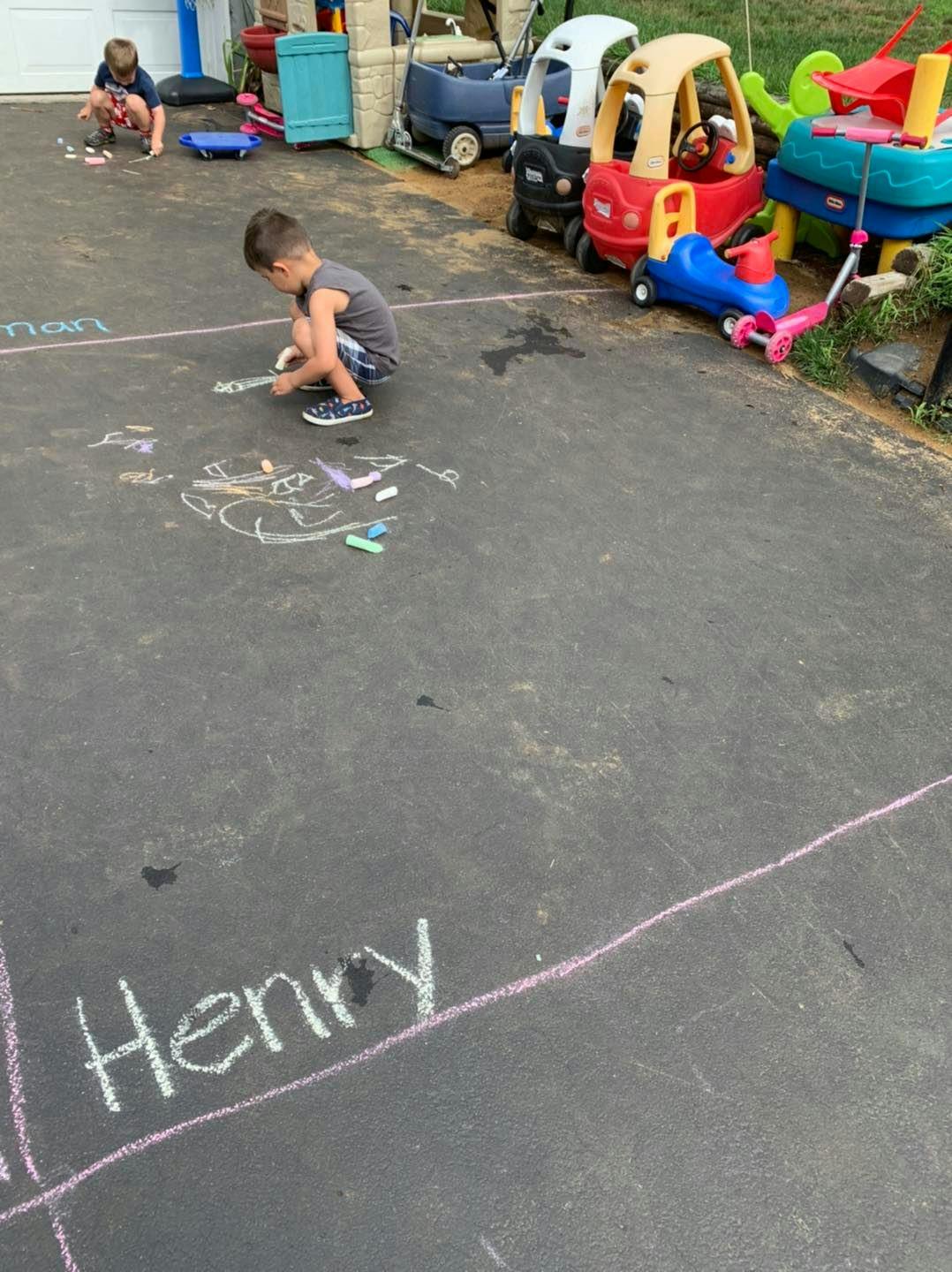 Child drawing with chalk on pavement, another child in background