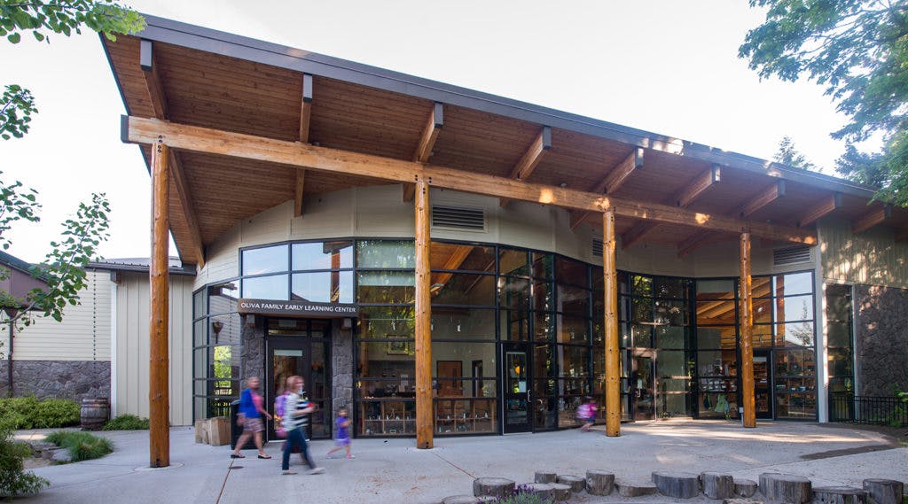 People and children entering a modern building with a large wooden overhang