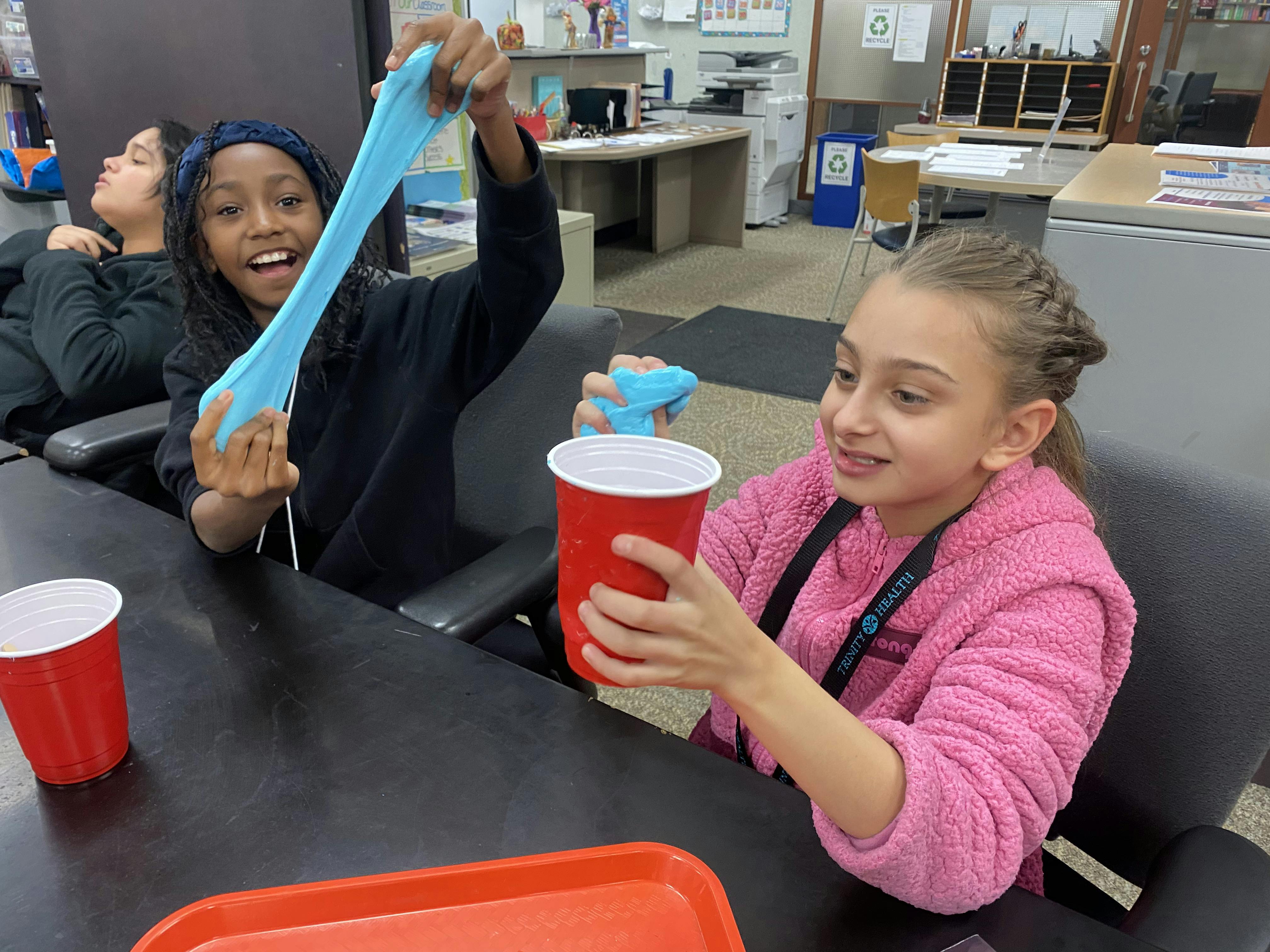 Two children playing with blue slime and red cups at a table