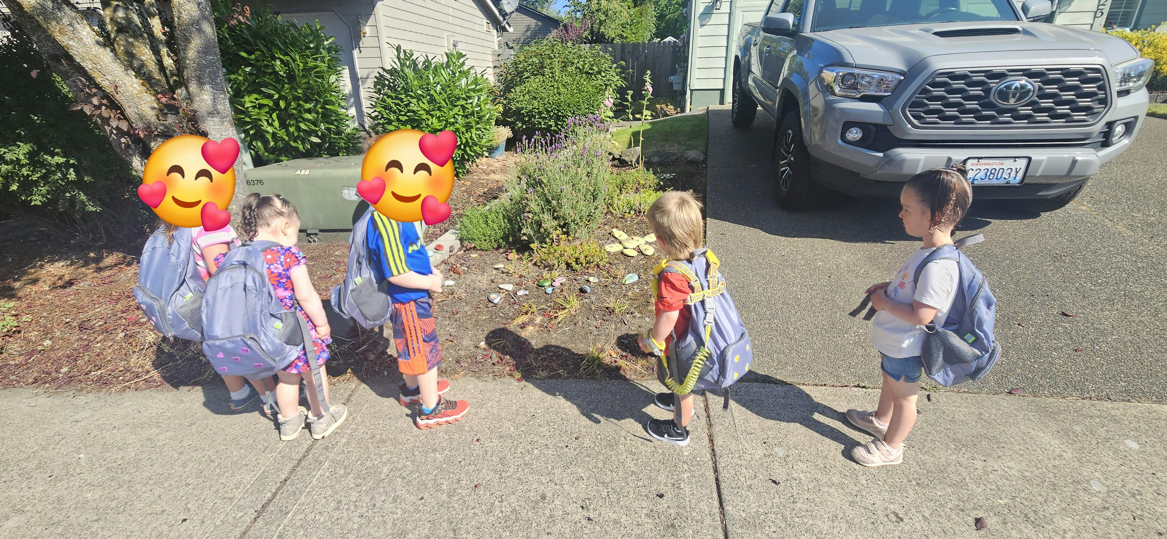 Four children with backpacks standing on a sidewalk