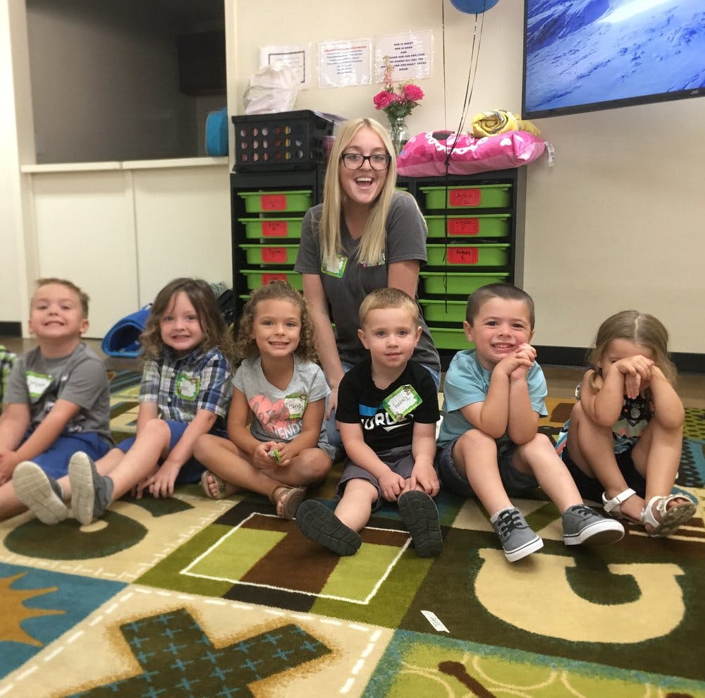 Person with glasses and five children sitting on a patterned rug