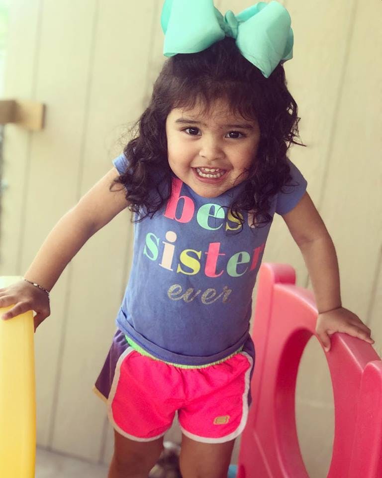 Child with a large bow in hair wearing a shirt that says "best sister ever"