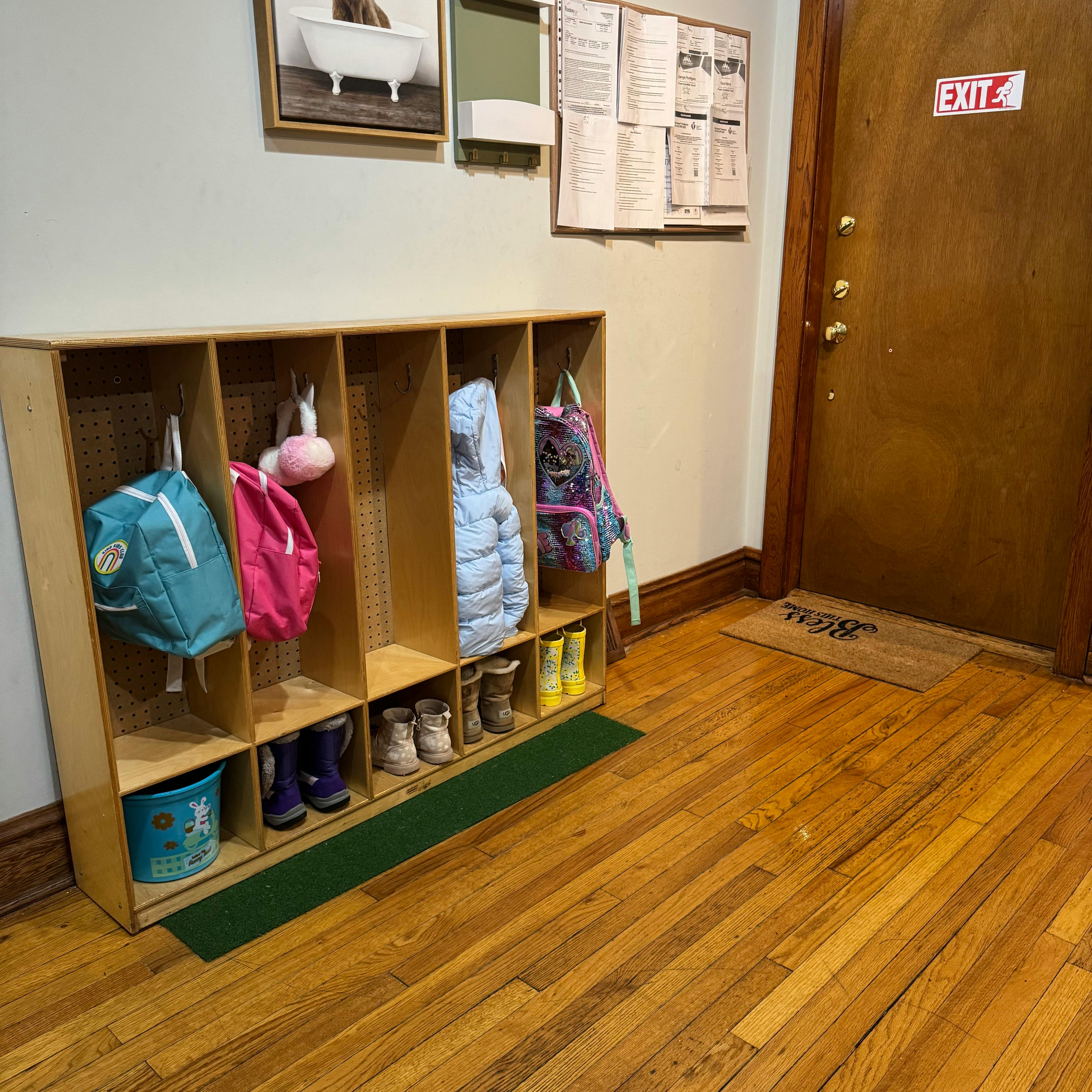 Cubby storage unit with backpacks and boots, next to a door with an exit sign