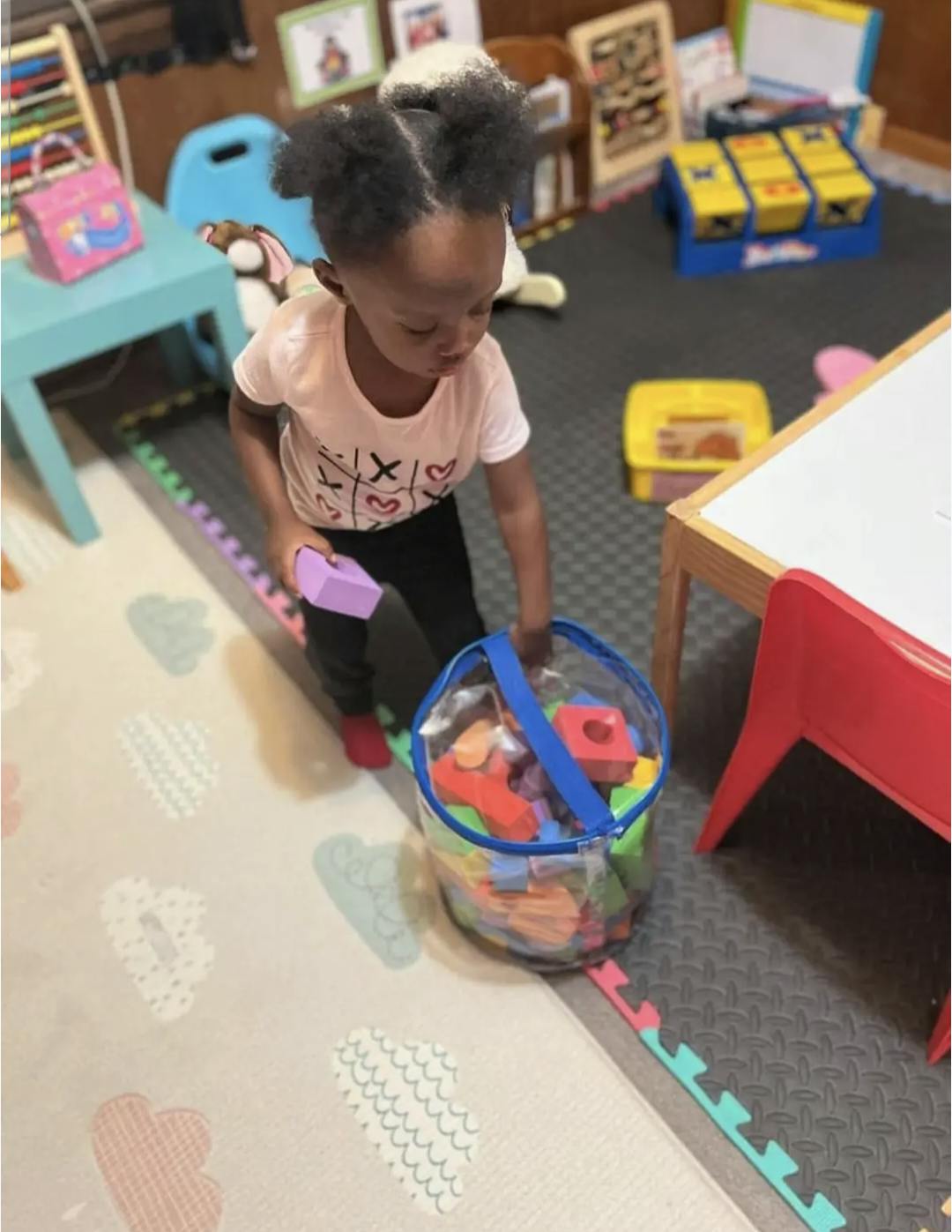 Child holding a purple block and a clear container of colorful blocks