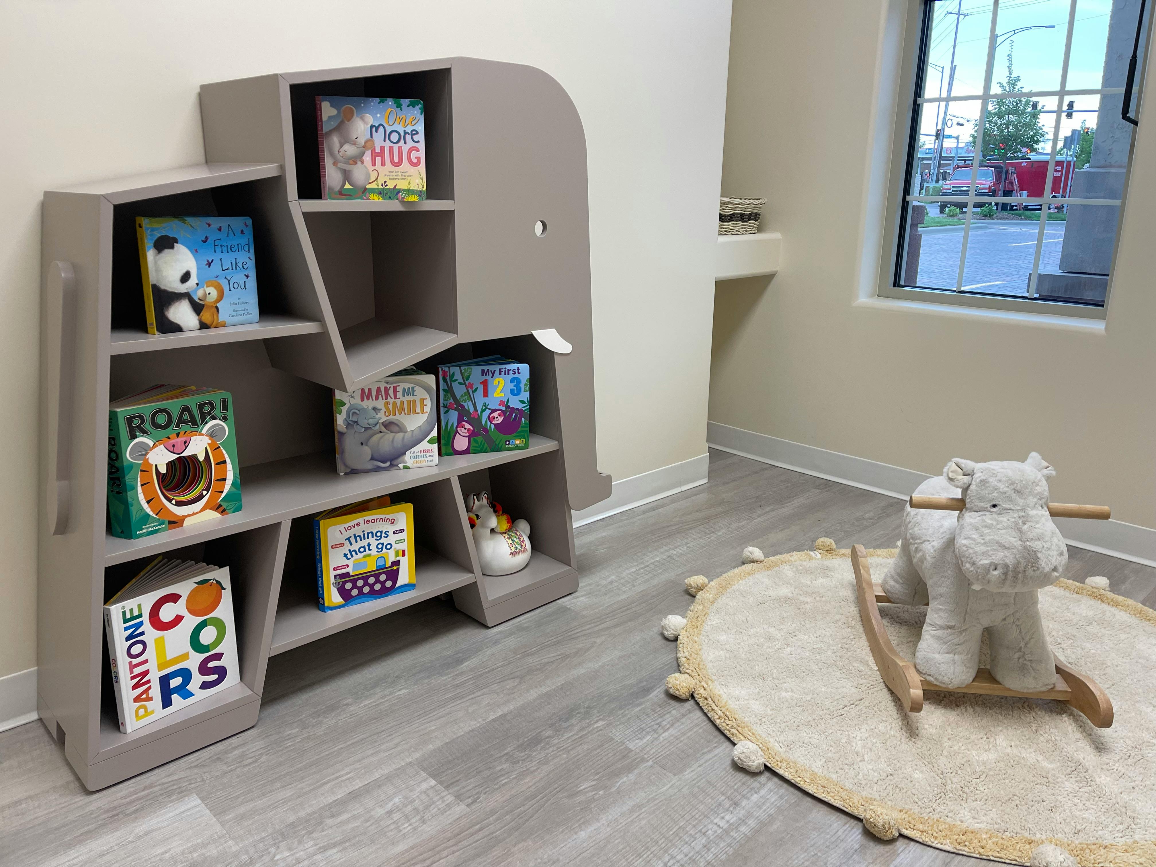 Bookshelf with books and a rocking horse on a rug in a room