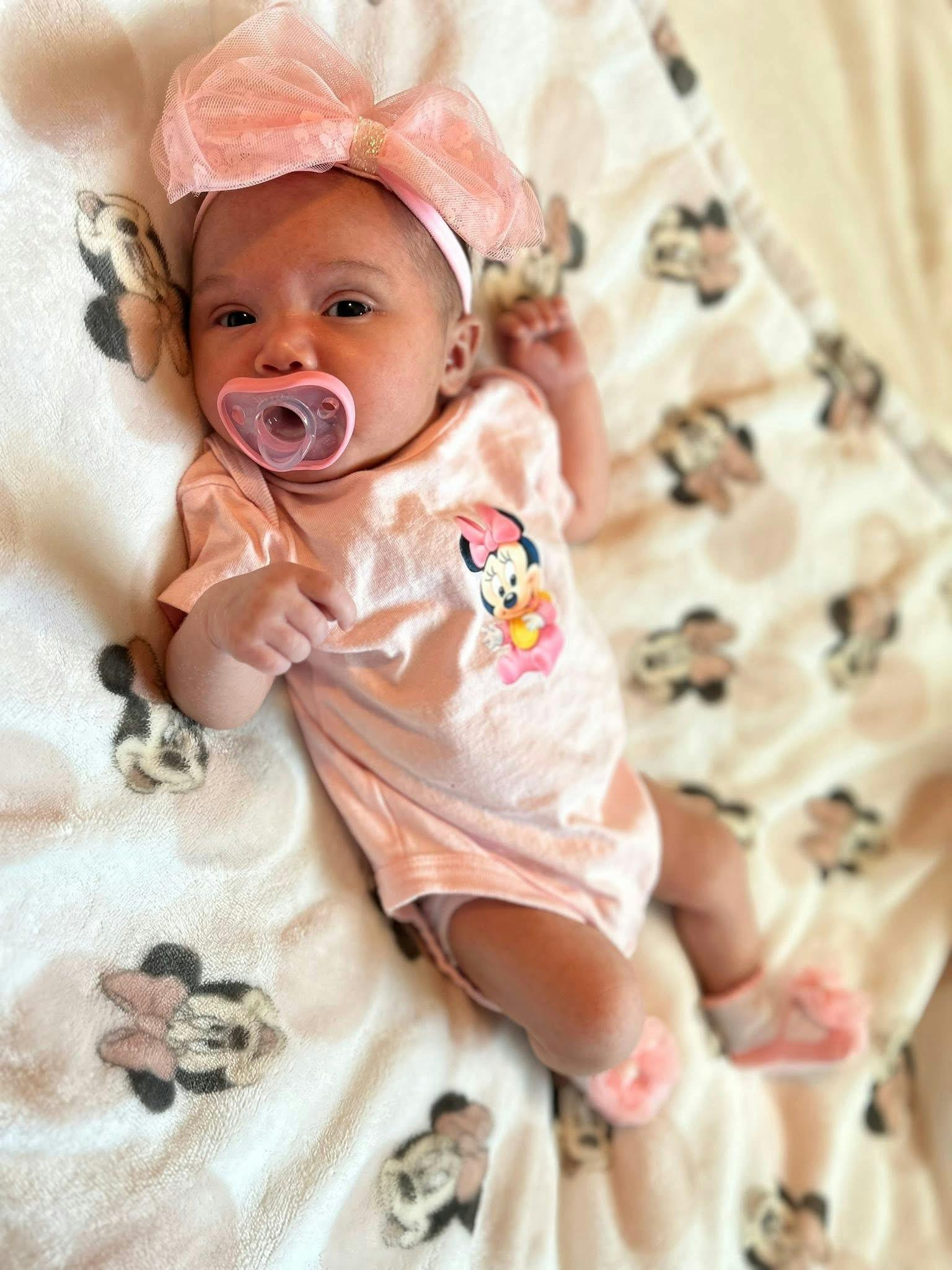 Baby wearing a headband and pacifier lying on a patterned blanket