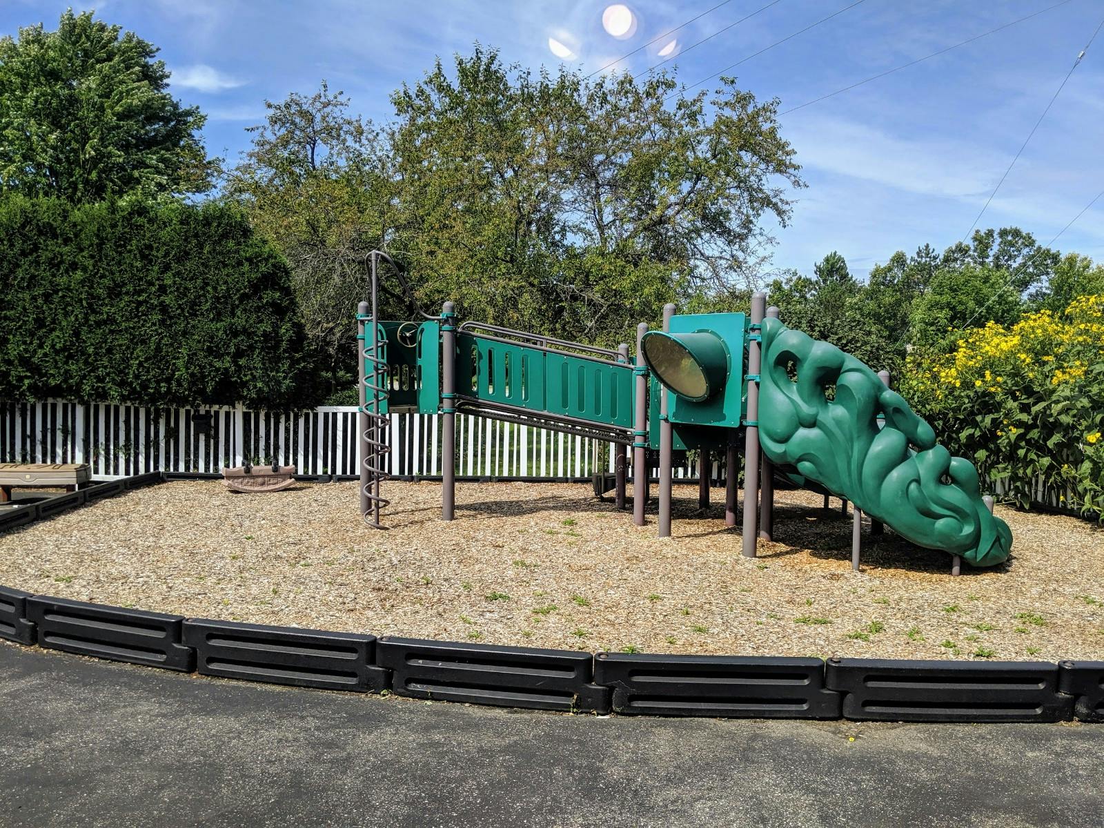 Playground with green slides and a white picket fence