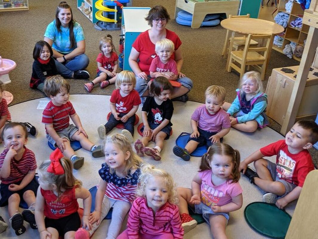 Two adults and many children sitting on the floor in a classroom