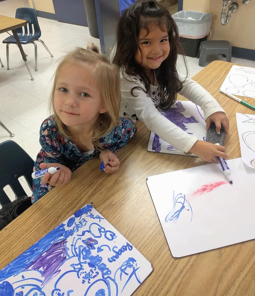 Two children drawing at a table in a classroom