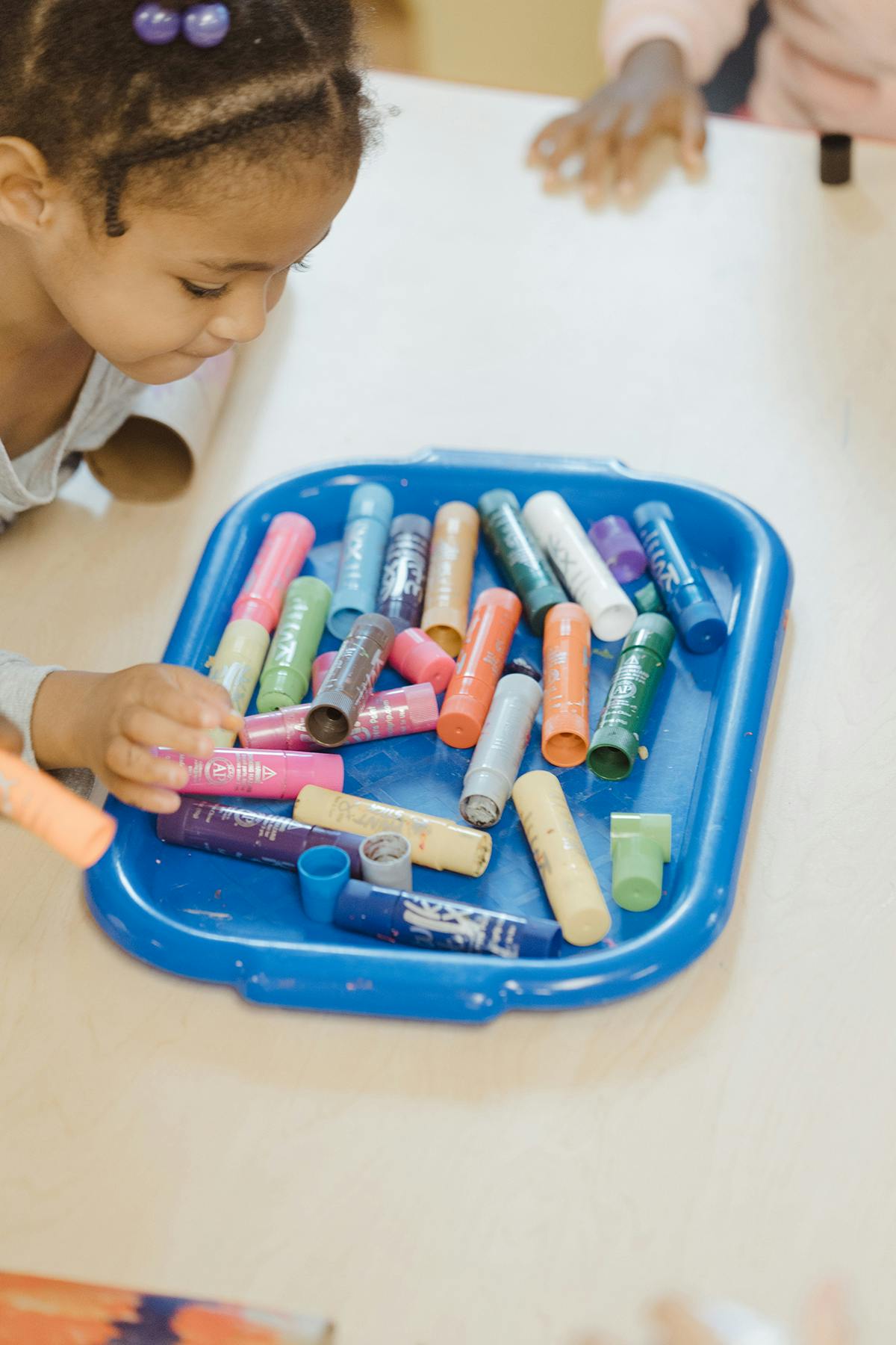 Child looking at a blue tray filled with colorful art supplies