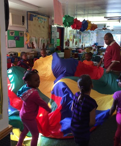 Adult and children playing with a colorful parachute in a classroom